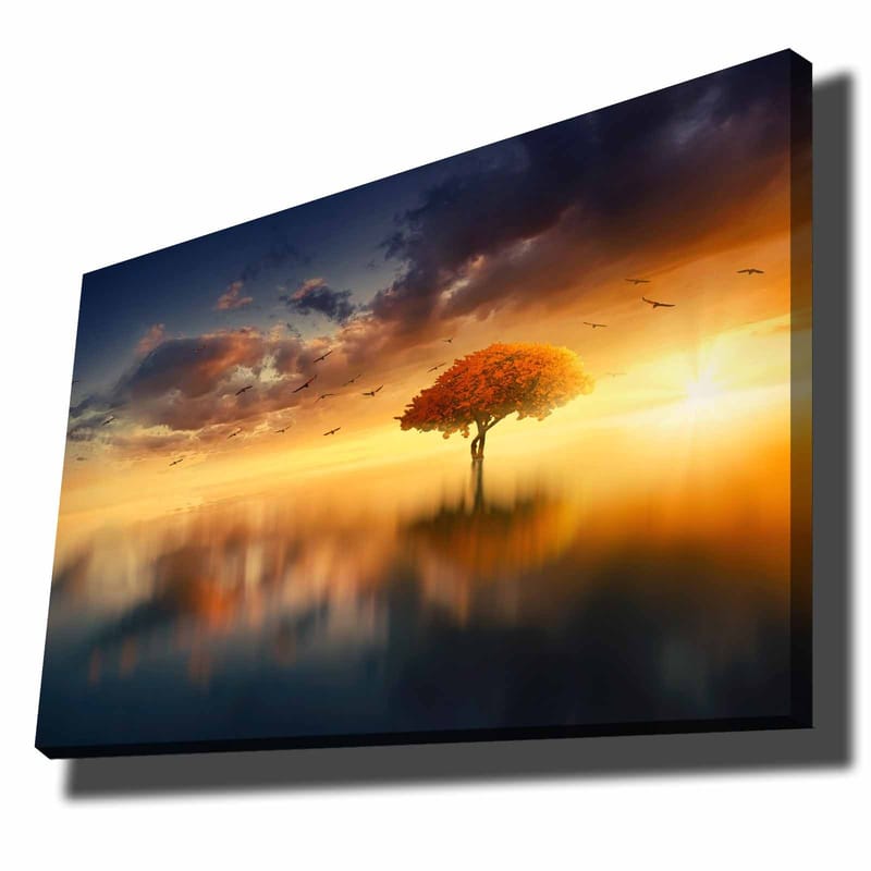 Lerretsbilde 70x100 cm - Et ensomt tre med en strålende oransje krone i et drømmeaktig landskap med solnedgang, Oransje / Blå / Gull