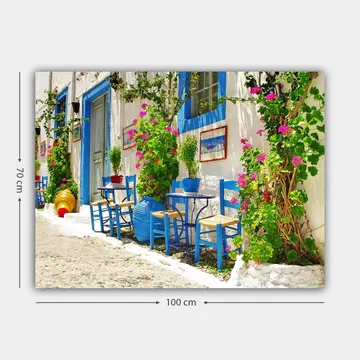 Lerretsbilde 70x100 cm - Fargerik og livlig gate med blå stoler og blomsterpotter i middelhavsmiljø - Blå / Grønn / Rosa - Interiør - Maleri & posters - Lerretsbilder