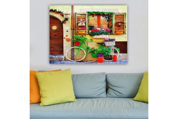 Lerretsbilde 70x100 cm - Fargerik sykkel pyntet med blomster og potter foran en sjarmerende vegg med vinduer og dekorasjoner - Grønn / Rosa / Oransje - Interiør - Maleri & posters - Lerretsbilder