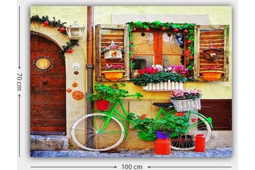 Lerretsbilde 70x100 cm - Fargerik sykkel pyntet med blomster og potter foran en sjarmerende vegg med vinduer og dekorasjoner - Grønn / Rosa / Oransje - Interiør - Maleri & posters - Lerretsbilder
