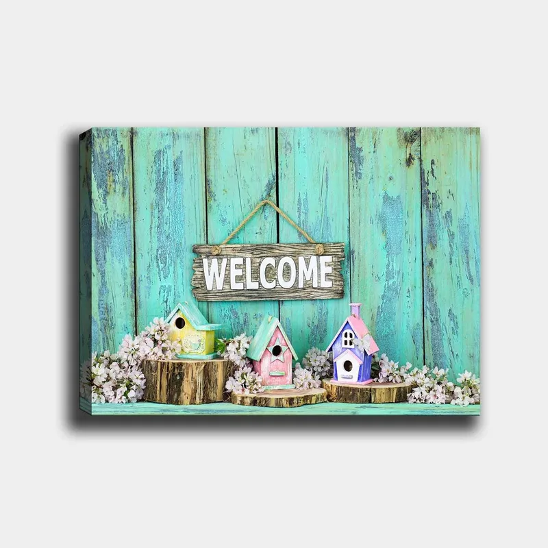 Lerretsbilde 70x100 cm - Fargerike fuglehus i et innbydende miljø med et treskilt, Turkis / Rosa / Gul