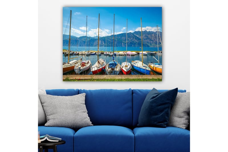 Lerretsbilde 70x100 cm - Flere fargerike seilbåter i en havn med fjell i bakgrunnen, Blå / Rød / Oransje