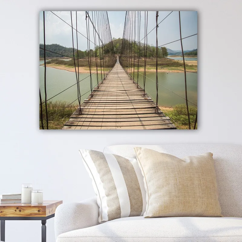 Lerretsbilde 70x100 cm - Hengebro som går over en rolig innsjø, omgitt av frodige, grønne åser, Grønn / Brun / Beige