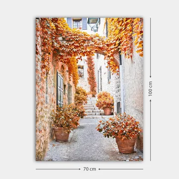 Lerretsbilde 70x100 cm - Malerisk smug omgitt av fargerike høstblader og potteplanter - Oransje / Brun / Gul - Interiør - Maleri & posters - Lerretsbilder