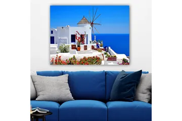 Lerretsbilde 70x100 cm - Malerisk utsikt over en hvitkalket bygning med en tradisjonell vindmølle og fargerike blomster på Santorini - Hvit / Blå / Rød - Interiør - Maleri & posters - Lerretsbilder