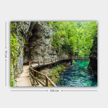 Lerretsbilde 70x100 cm - Naturskjønn utsikt over en trebro som slynger seg gjennom en frodig kløft ved en klar, turkis elv - Grønn / Turkis / Grå - Interiør - Maleri & posters - Lerretsbilder