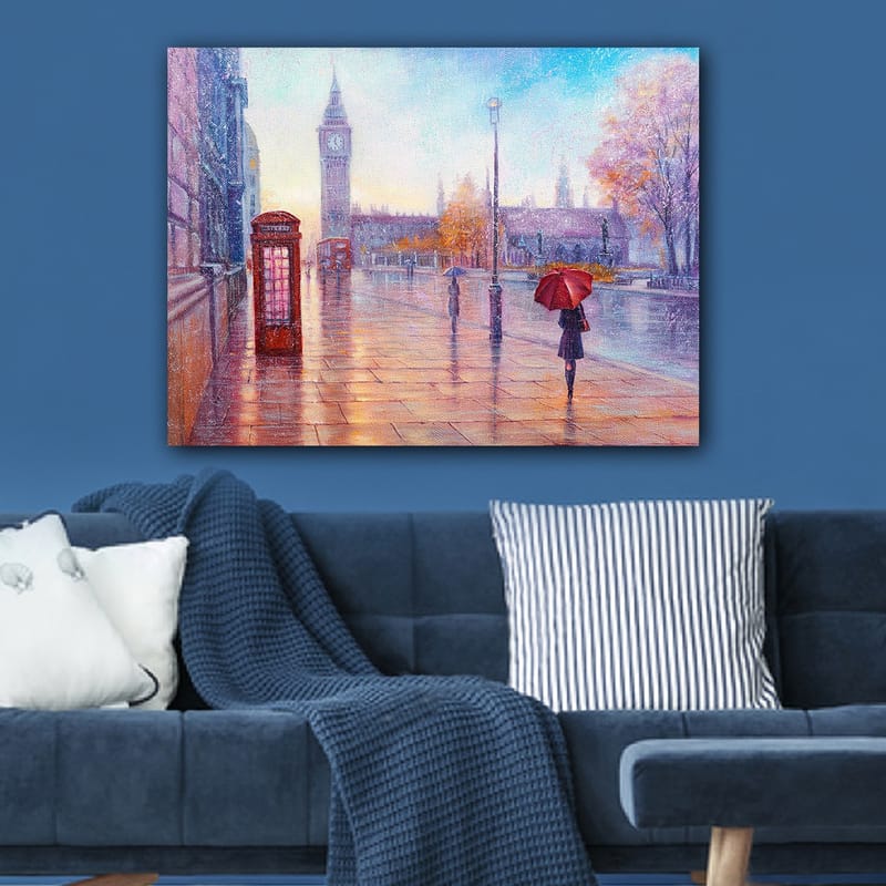 Lerretsbilde 70x100 cm - Regnfullt bybilde med en rød telefonkiosk og en person med en rød paraply som går langs en våt gate - Rød / Blå / Oransje - Interiør - Maleri & posters - Lerretsbilder