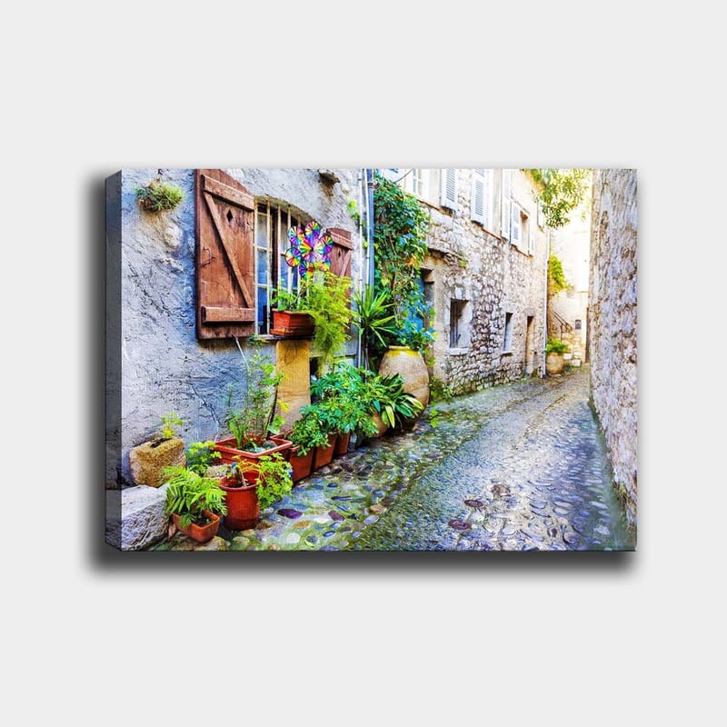 Lerretsbilde 70x100 cm - Sjarmerende smug med steinhus og blomsterpotter som skaper en livlig atmosfære, Grønn / Blå / Beige