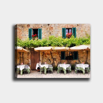 Lerretsbilde 70x100 cm - Sjarmerende utendørs spiseplass med hvite bord og grønne duker foran en gammel steinbygning med mørkegrønne skodder - Mørkegrønn / Hvit / Mursteinsrød - Interiør - Maleri & posters - Lerretsbilder