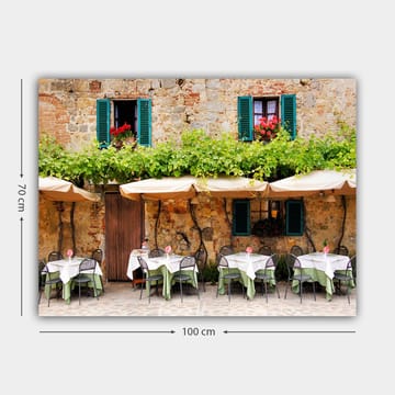 Lerretsbilde 70x100 cm - Sjarmerende utendørs spiseplass med hvite bord og grønne duker foran en gammel steinbygning med mørkegrønne skodder - Mørkegrønn / Hvit / Mursteinsrød - Interiør - Maleri & posters - Lerretsbilder