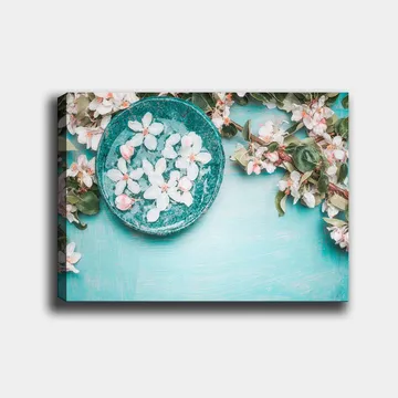 Lerretsbilde 70x100 cm - Skål med blomster omgitt av frodige grønne kvister og blomster på en lyseblå bakgrunn - Turkis / Hvit / Rosa - Interiør - Maleri & posters - Lerretsbilder