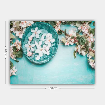 Lerretsbilde 70x100 cm - Skål med blomster omgitt av frodige grønne kvister og blomster på en lyseblå bakgrunn - Turkis / Hvit / Rosa - Interiør - Maleri & posters - Lerretsbilder