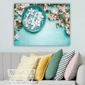 Lerretsbilde 70x100 cm - Skål med blomster omgitt av frodige grønne kvister og blomster på en lyseblå bakgrunn - Turkis / Hvit / Rosa - Interiør - Maleri & posters - Lerretsbilder