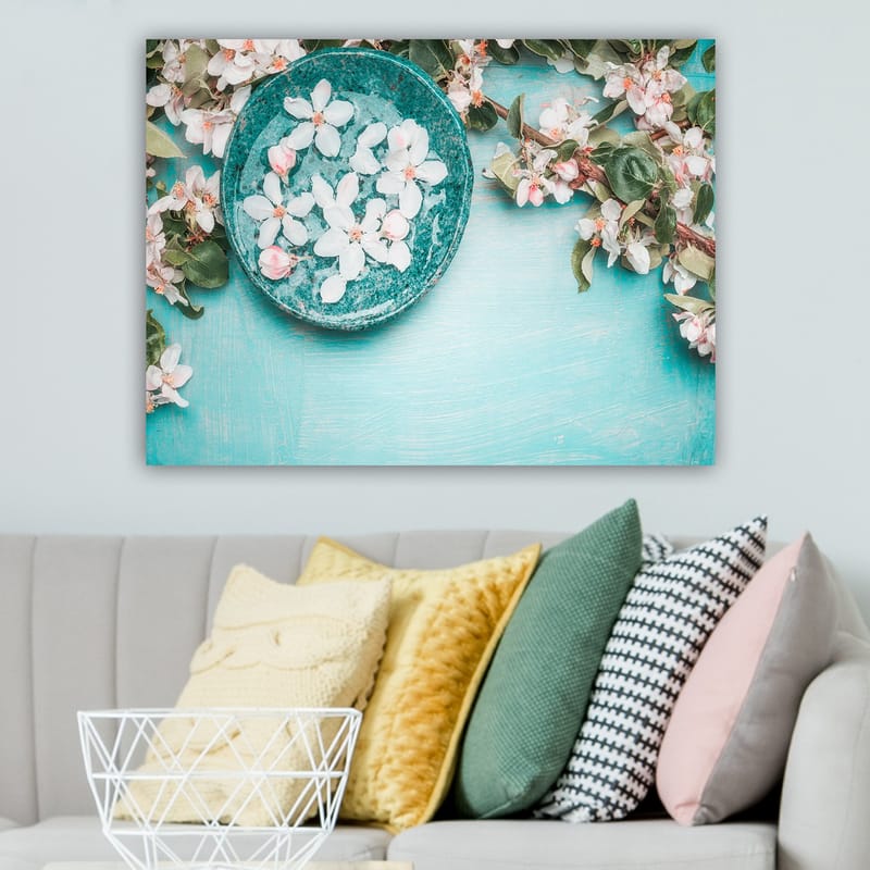 Lerretsbilde 70x100 cm - Skål med blomster omgitt av frodige grønne kvister og blomster på en lyseblå bakgrunn - Turkis / Hvit / Rosa - Interiør - Maleri & posters - Lerretsbilder