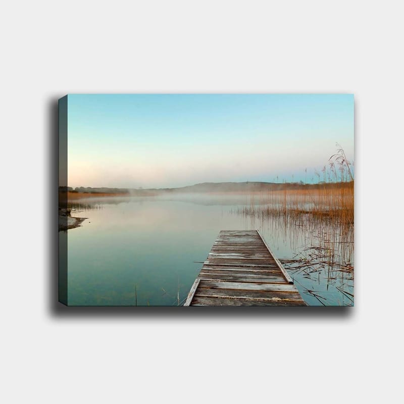 Lerretsbilde 70x100 cm - Stille brygge som strekker seg ut over en tåkete innsjø ved daggry, Lys blå / Beige / Grønn