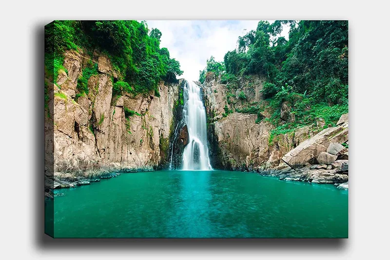 Lerretsbilde 70x100 cm - Storslått foss som fosser ned i en klar, turkis innsjø omgitt av frodige, grønne klipper, Turkis / Grønn / Beige