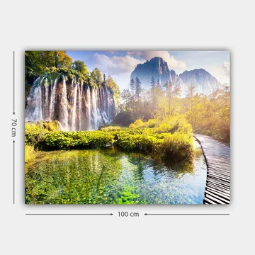 Lerretsbilde 70x100 cm - Storslått fossefall omgitt av frodig vegetasjon og majestetiske fjell - Grønn / Blå / Gul - Interiør - Maleri & posters - Lerretsbilder