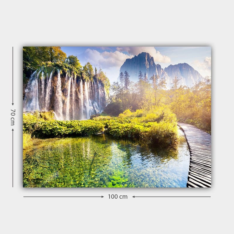 Lerretsbilde 70x100 cm - Storslått fossefall omgitt av frodig vegetasjon og majestetiske fjell - Grønn / Blå / Gul - Interiør - Maleri & posters - Lerretsbilder