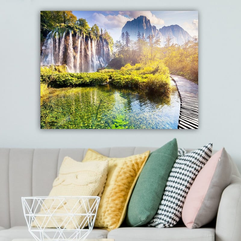 Lerretsbilde 70x100 cm - Storslått fossefall omgitt av frodig vegetasjon og majestetiske fjell - Grønn / Blå / Gul - Interiør - Maleri & posters - Lerretsbilder