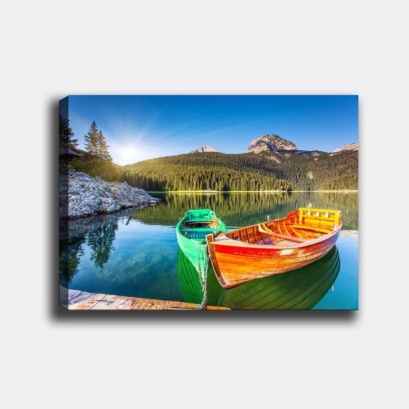 Lerretsbilde 70x100 cm - To fargerike båter ligger stille på en speilblank innsjø omgitt av frodige fjell, Grønn / Oransje / Blå