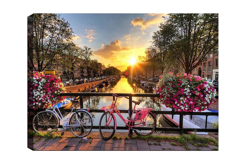 Lerretsbilde 70x100 cm - To sykler i pittoresk kanalsetting med blomster og solnedgang, Rosa / Hvit / Grønn