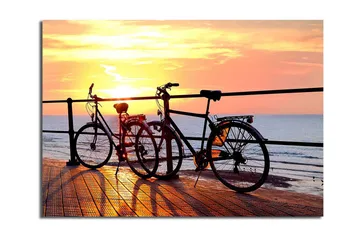 Lerretsbilde 70x100 cm - To sykler som står på en brygge ved solnedgang over havet - Oransje / Svart / Gul - Interiør - Maleri & posters - Lerretsbilder