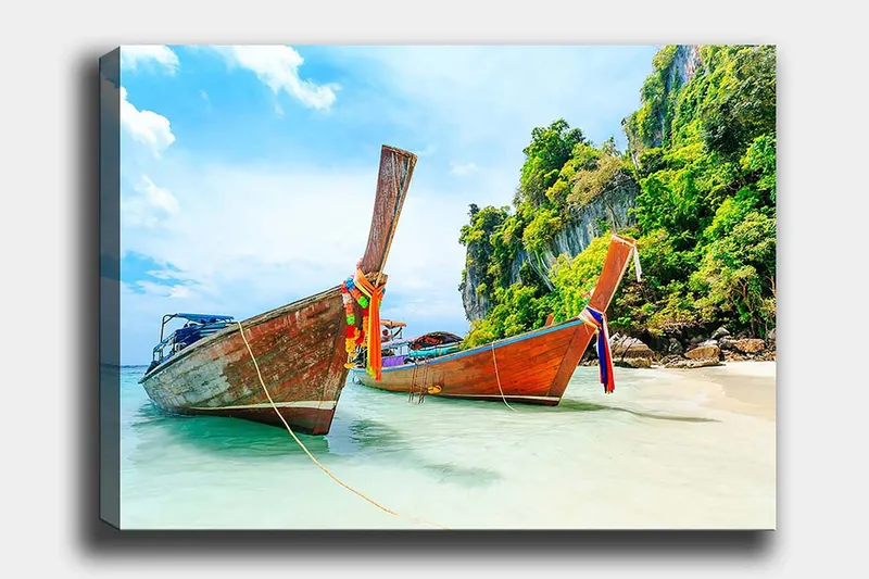 Lerretsbilde 70x100 cm - To tradisjonelle thailandske langbåter på en strand med steiner og frodig vegetasjon i bakgrunnen, Brun / Grønn / Blå