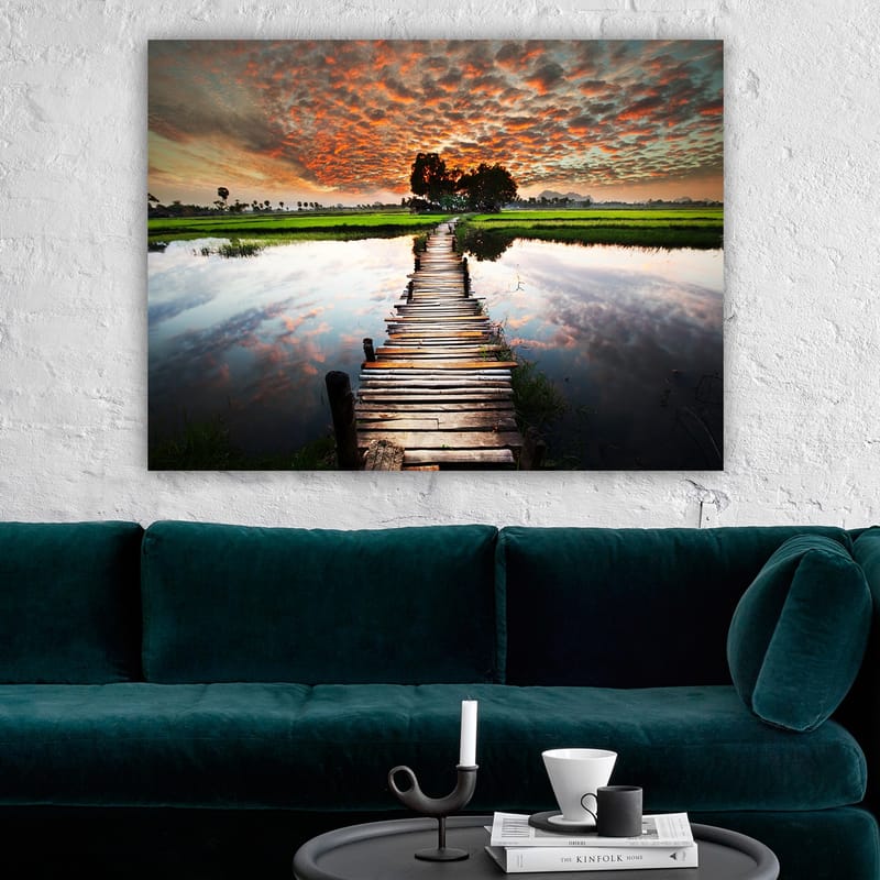 Lerretsbilde 70x100 cm - Trebro som spenner over en speilblank vannoverflate, omgitt av frodig grøntområde og en dramatisk solnedgang - Oransje / Grønn / Blå - Interiør - Maleri & posters - Lerretsbilder