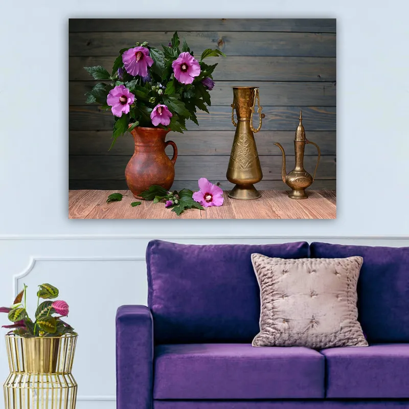 Lerretsbilde 70x100 cm - Vakker bukett med rosa blomster i en keramisk vase på et trebord, omgitt av metallgjenstander, Rosa / Grønn / Brun