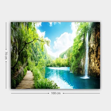 Lerretsbilde 70x100 cm - Vakker naturscene med en foss som renner ut i en klar, blå innsjø omgitt av frodig grøntområde og fjell - Grønn / Blå - Interiør - Maleri & posters - Lerretsbilder