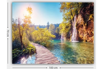 Lerretsbilde 70x100 cm - Vakker naturutsikt med en trebro som fører gjennom frodig grøntområde og en foss i bakgrunnen - Grønn / Blå / Gul - Interiør - Maleri & posters - Lerretsbilder