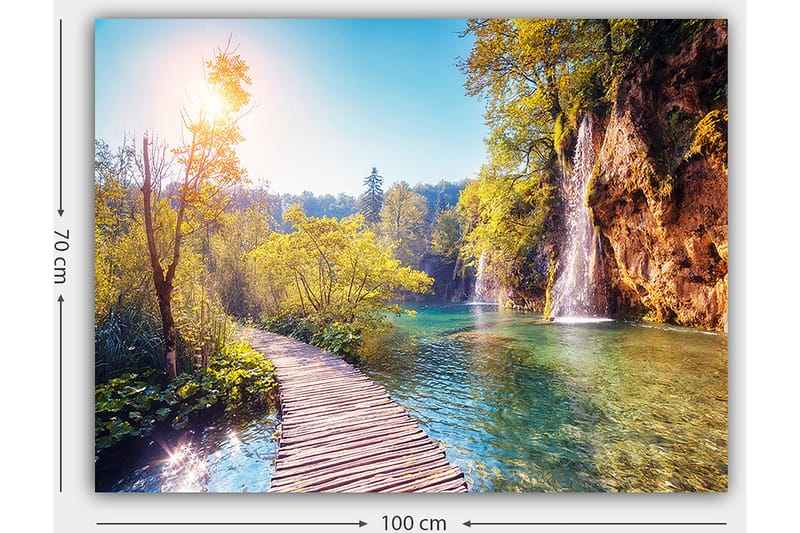 Lerretsbilde 70x100 cm - Vakker naturutsikt med en trebro som fører gjennom frodig grøntområde og en foss i bakgrunnen - Grønn / Blå / Gul - Interiør - Maleri & posters - Lerretsbilder