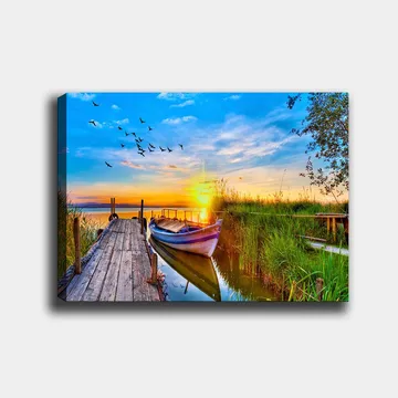 Lerretsbilde 70x100 cm - Vakker solnedgang over en rolig innsjø med en båt ved en trebrygge omgitt av grøntområder - Blå / Oransje / Grønn - Interiør - Maleri & posters - Lerretsbilder