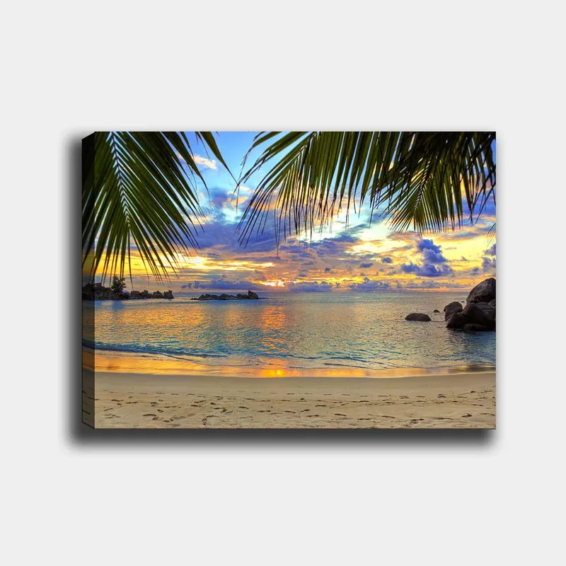 Lerretsbilde 70x100 cm - Vakker solnedgang over en strand med palmer som rammer inn motivet, Blå / Oransje / Grønn