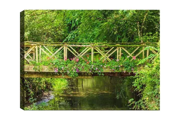 Lerretsbilde 70x100 cm - Vakker trebro omgitt av grøntområder og blomster ved en rolig vannflate - Grønn / Rosa / Brun - Interiør - Maleri & posters - Lerretsbilder