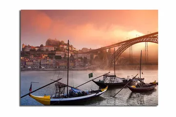 Lerretsbilde 70x100 cm - Vakker utsikt over elven med tradisjonelle båter og en majestetisk bro i bakgrunnen, omgitt av fargerike hus - Oransje / Blå / Gul - Interiør - Maleri & posters - Lerretsbilder