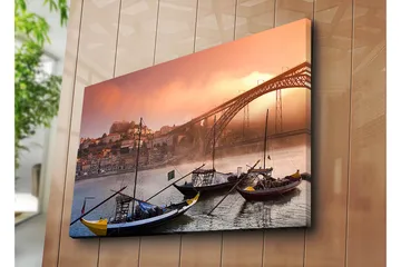 Lerretsbilde 70x100 cm - Vakker utsikt over elven med tradisjonelle båter og en majestetisk bro i bakgrunnen, omgitt av fargerike hus - Oransje / Blå / Gul - Interiør - Maleri & posters - Lerretsbilder