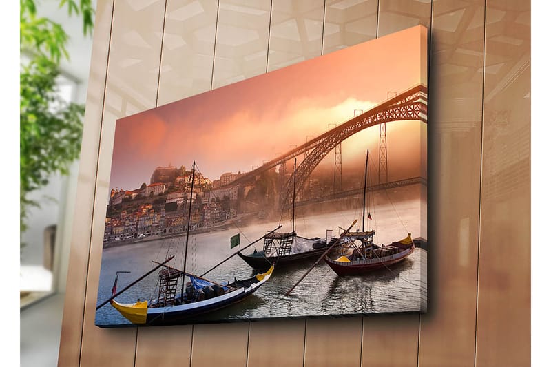 Lerretsbilde 70x100 cm - Vakker utsikt over elven med tradisjonelle båter og en majestetisk bro i bakgrunnen, omgitt av fargerike hus - Oransje / Blå / Gul - Interiør - Maleri & posters - Lerretsbilder