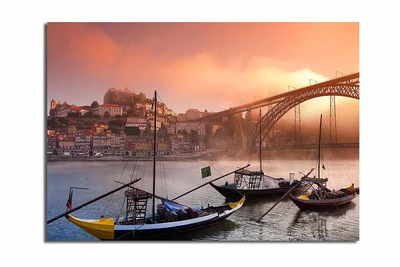 Lerretsbilde 70x100 cm - Vakker utsikt over elven med tradisjonelle båter og en majestetisk bro i bakgrunnen, omgitt av fargerike hus, Oransje / Blå / Gul
