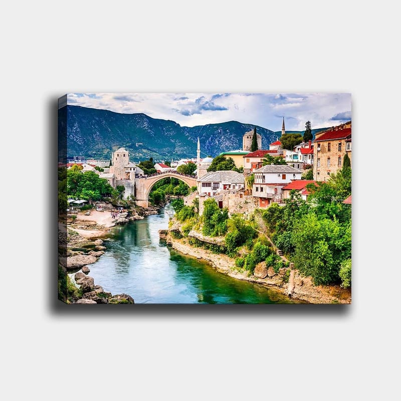 Lerretsbilde 70x100 cm - Vakker utsikt over en historisk bro som krysser en elv, omgitt av pittoreske hus og frodig grøntområde, Grønn / Blå / Rød