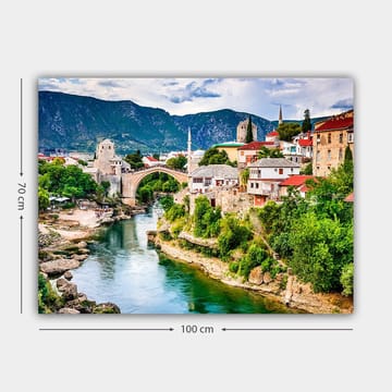 Lerretsbilde 70x100 cm - Vakker utsikt over en historisk bro som krysser en elv, omgitt av pittoreske hus og frodig grøntområde - Grønn / Blå / Rød - Interiør - Maleri & posters - Lerretsbilder