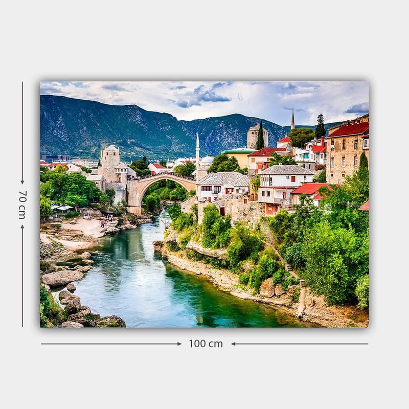 Lerretsbilde 70x100 cm - Vakker utsikt over en historisk bro som krysser en elv, omgitt av pittoreske hus og frodig grøntområde - Grønn / Blå / Rød - Interiør - Maleri & posters - Lerretsbilder