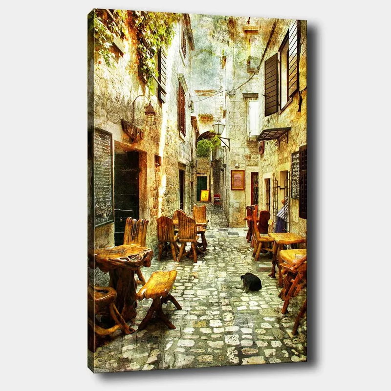 Lerretsbilde 70x100 cm - Pittoresk smug med trebord og stoler, omgitt av gamle steinhus, Brun / Grå / Grønn