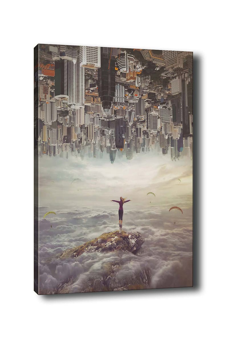 Lerretsbilde 70x100 cm - Person som står med utstrakte armer på en klippe over skyene, med en by i bakgrunnen som er opp ned, Grå / Beige / Mørk blå