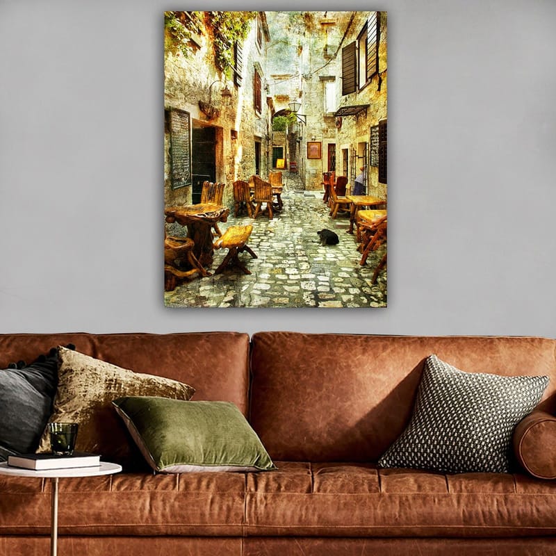 Lerretsbilde 70x100 cm - Pittoresk smug med trebord og stoler, omgitt av gamle steinhus - Brun / Grå / Grønn - Interiør - Maleri & posters - Lerretsbilder