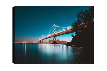 Lerretsbilde - Opplyst bro over en stille vannflate med byens skyline i bakgrunnen - Blå / Oransje / Svart - Interiør - Maleri & posters - Lerretsbilder